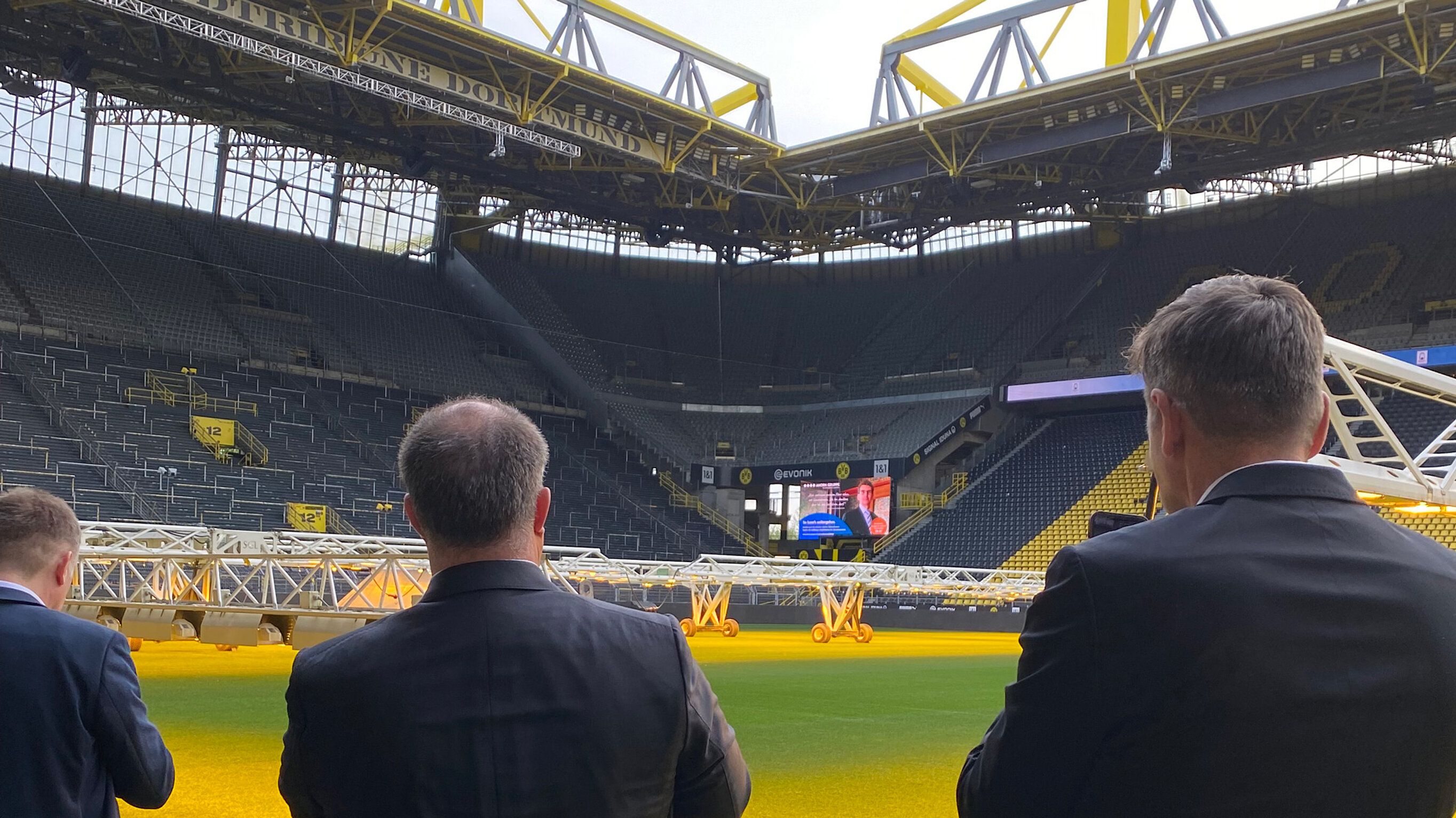 Hinter den Rücken von zwei Männern ist der Innenraum eines Fußballstadions zu sehen.